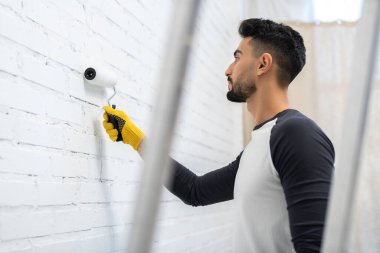 Side view of muslim man painting white brick wall at home 