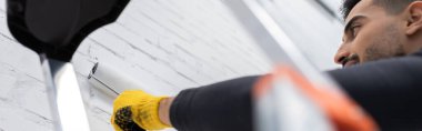 Low angle view of muslim man coloring brick wall at home, banner 