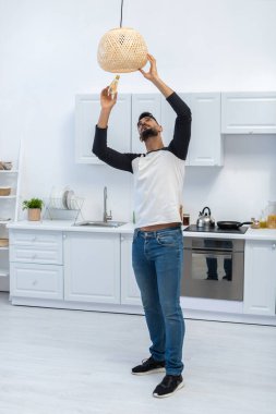 Arabian man holding lightbulb near chandelier in kitchen 