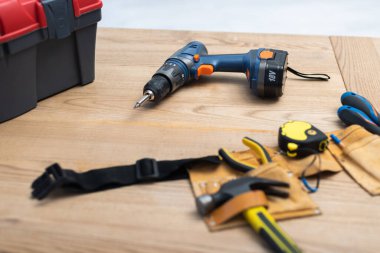 Electric screwdriver near tool belt on table at home 