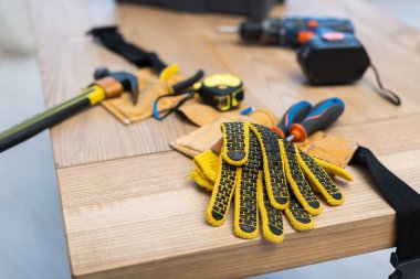 Gloves near blurred belt with tools on table at home 