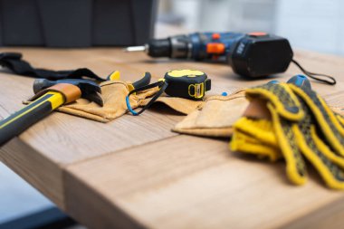 Hammer and tape measure on belt near blurred gloves on table 