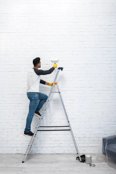 Arabian Man Coloring Brick Wall While Standing Ladder Living Room — Fotografia de Stock