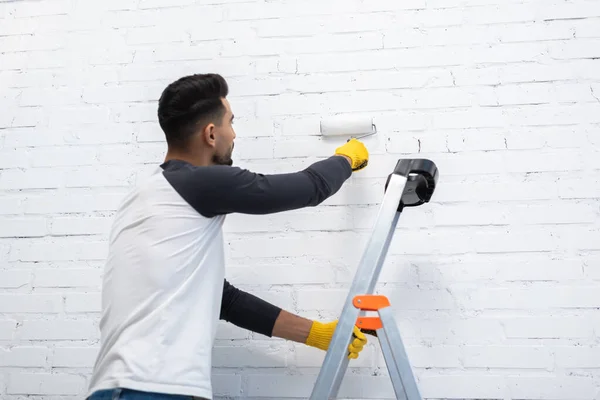 Young Muslim Man Painting Wall Roller While Standing Ladder Living — Stockfoto