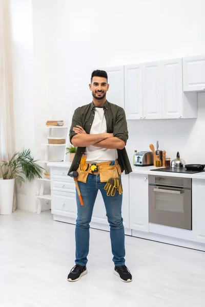 Cheerful Muslim Man Tool Belt Crossing Arms Kitchen — Zdjęcie stockowe