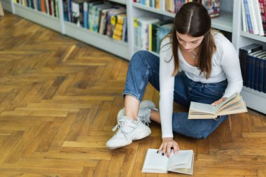 high angle view of teenage girl with books sitting on floor in library