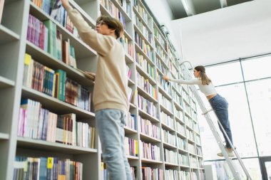 low angle view of teenage students choosing books on shelves in library