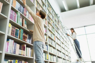 low angle view of students choosing books from variety on racks in library