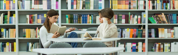 teen girl holding book while talking to guy in library, banner