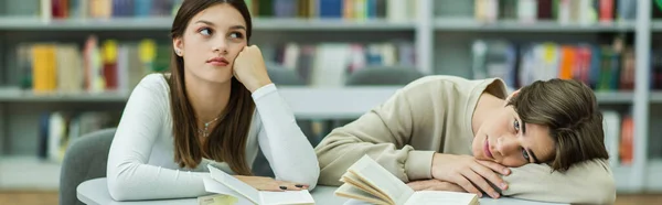 bored guy looking at camera near pensive teenage girl in reading room, banner