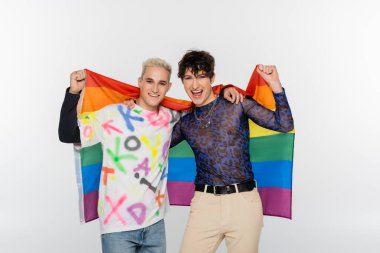 excited queer person and happy gay man holding lgbt flag and looking at camera isolated on grey