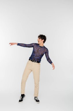 full length of amazed queer person looking away and pointing with hand on grey background