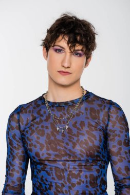 young queer person with trendy hairstyle and makeup looking at camera isolated on grey
