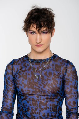 nonbinary model with wavy hair and makeup looking at camera isolated on grey