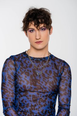 brunette queer model in long sleeve shirt and silver necklaces isolated on grey