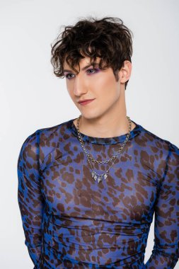 brunette queer model in long sleeve shirt and silver necklaces isolated on grey
