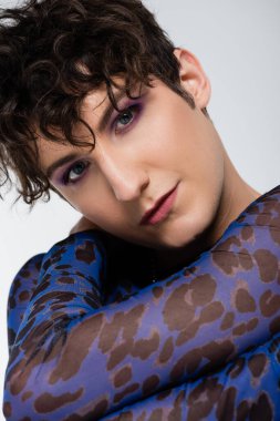 portrait of nonbinary model with trendy hairstyle and makeup looking at camera isolated on grey