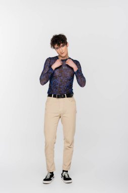 full length of brunette queer model touching silver necklaces on grey background