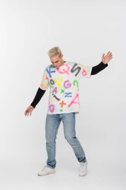 full length of gay man in alphabet print t-shirt posing on grey background