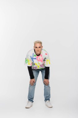 full length of blonde gay man in trendy clothes looking at camera on grey background