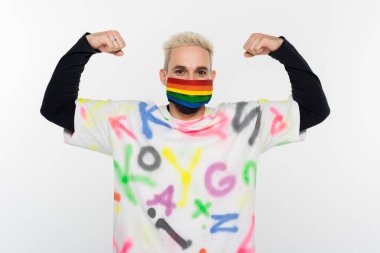 gay man in rainbow colors medical mask demonstrating strength isolated on grey