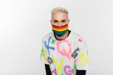 young gay in rainbow colors medical mask and trendy t-shirt looking at camera isolated on grey