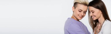 pretty and trendy lesbian couple with makeup smiling isolated on grey, banner