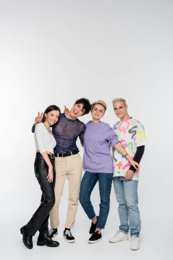 happy queer person showing victory sign near diverse lgbtq friends on grey background