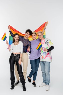 cheerful friends of diverse identity standing with lgbtq flags on grey background