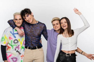 happy lesbian woman waving hand near lgbtq community friends embracing isolated on grey