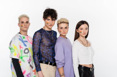 young friends with lgbtq flags on faces looking at camera isolated on grey