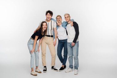 full length of young and stylish friends laughing on grey background