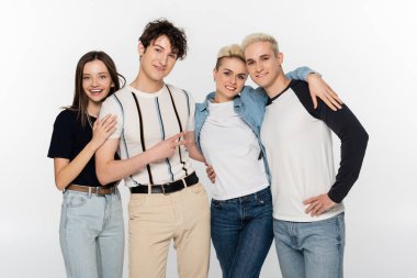 young man showing peace gesture near stylish friends embracing isolated on grey