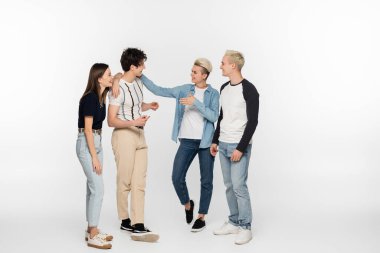 full length of stylish and cheerful friends gesturing during conversation on grey background