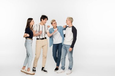 trendy man pointing with finger while talking to smiling friends on grey background