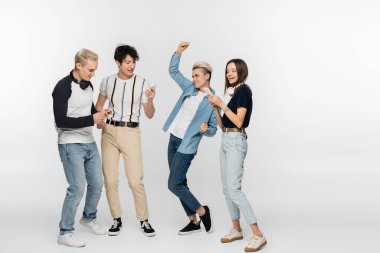 young woman dancing near friends with mobile phones on grey background