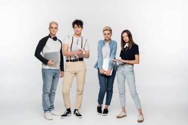 full length of young friends with laptops and digital tablets on grey background