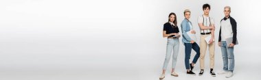 full length of young people with digital tablets and laptops looking at camera on grey background, banner
