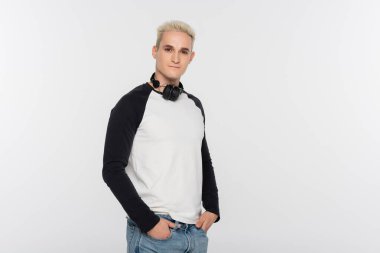 trendy man in black and white long sleeve shirt standing with wireless headphones isolated on grey