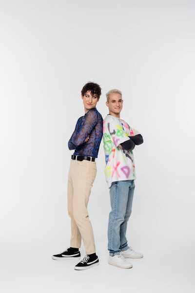full length of trendy gay man and queer person standing back to back with crossed arms on grey background