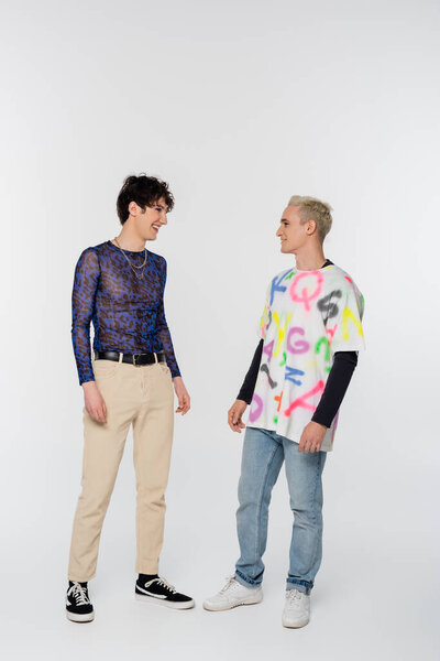 full length of happy gay man and queer person looking at each other on grey background