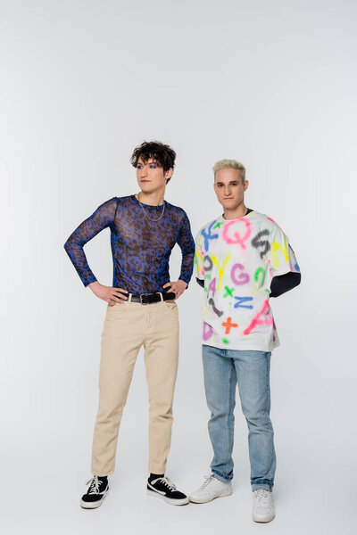 full length of queer person and gay man posing on grey background