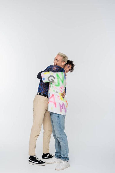 side view of young and stylish gay and queer person embracing on grey background