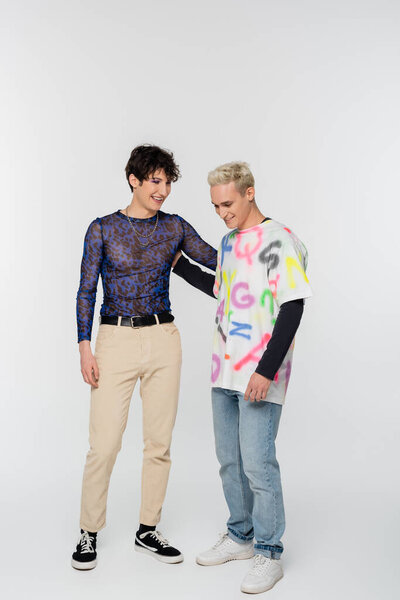 young and happy gay and nonbinary person hugging on grey background