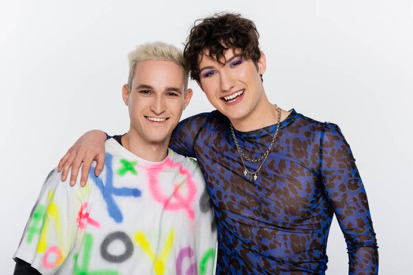 happy nonbinary person embracing smiling gay man and looking at camera isolated on grey