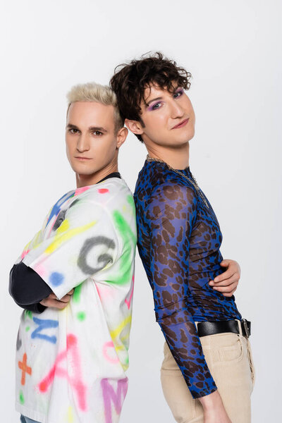 blonde gay man and brunette nonbinary person in stylish clothes standing back to back isolated on grey