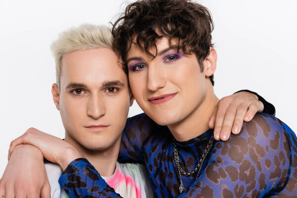 smiling queer person with makeup embracing blonde gay man isolated on grey