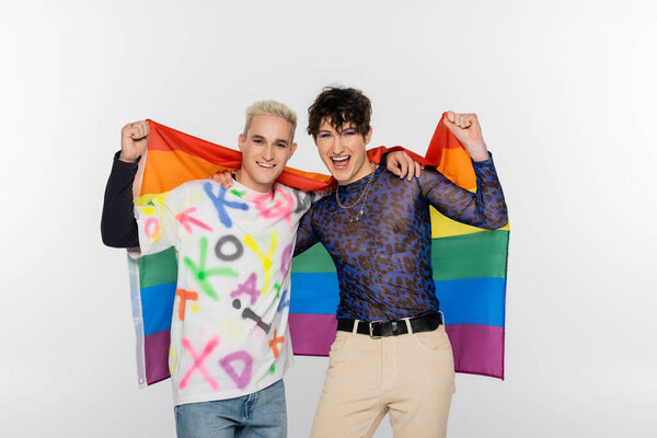 excited queer person and happy gay man holding lgbt flag and looking at camera isolated on grey
