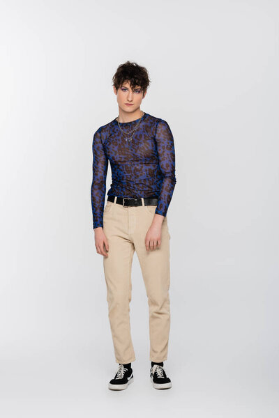 full length of young nonbinary person in stylish clothes standing on grey background