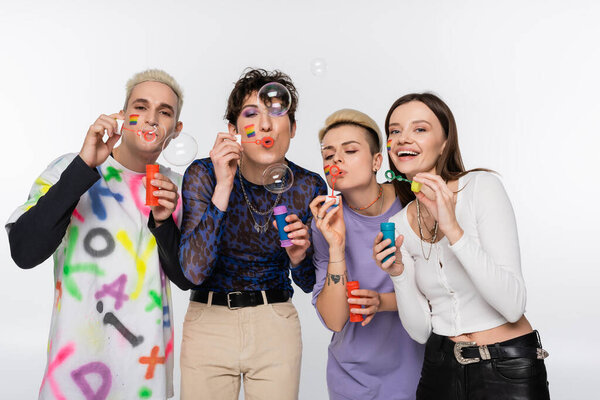 young people with lgbtq flags on faces blowing soap bubbles isolated on grey